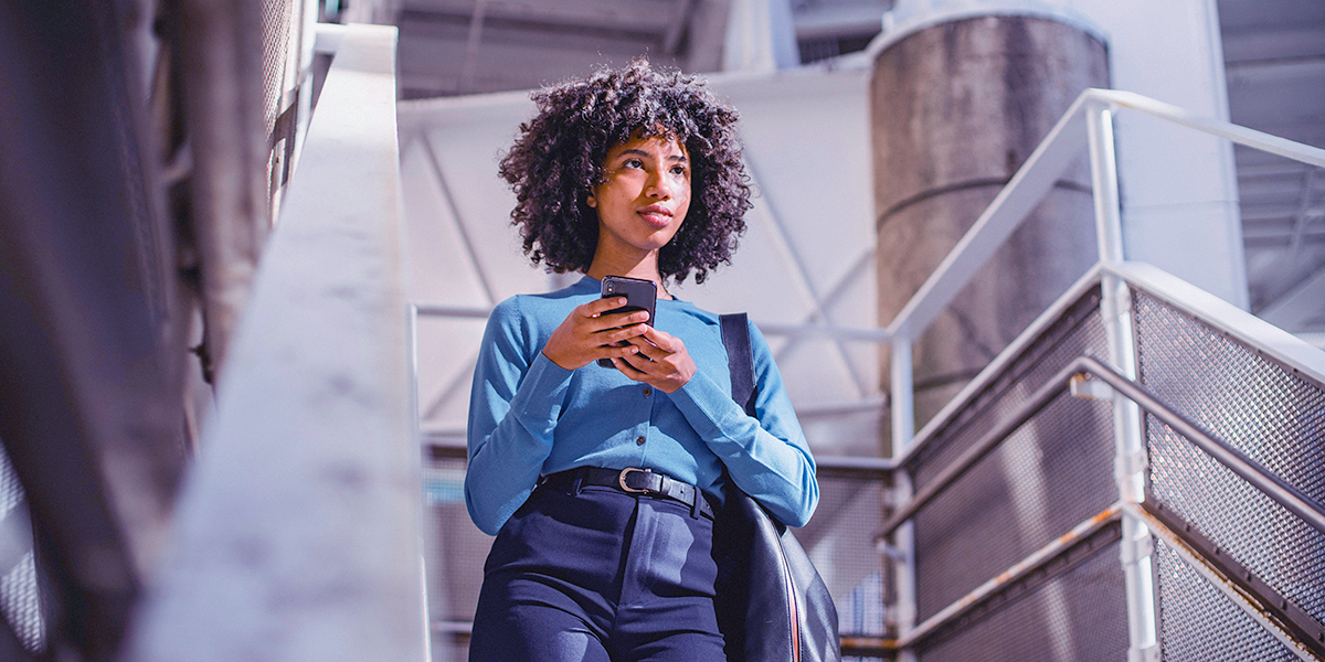 Young woman holding phone, walking down stairs to her new job