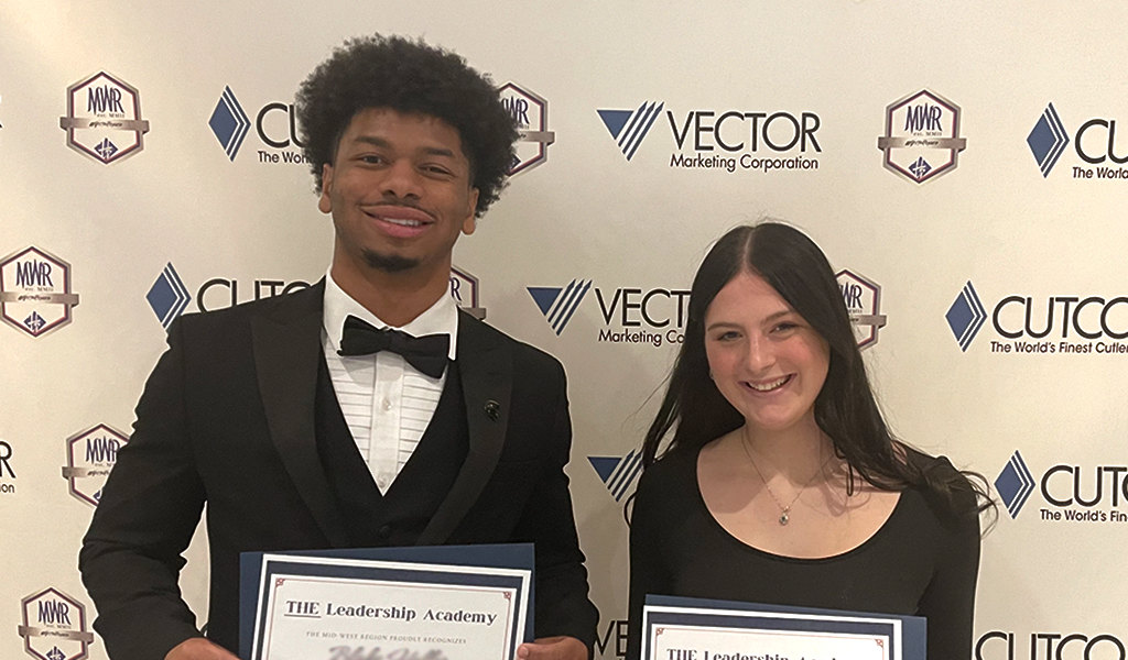 Young man and young woman, Vector sales representatives, holding awards in front of a Vector/Cutco background
