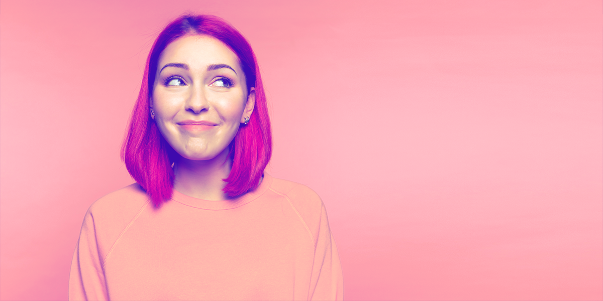 Young woman with pink hair look up and to the side, smiling uncertainly