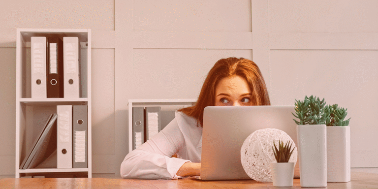 Young woman task masking and hiding behind her computer, trying to look productive