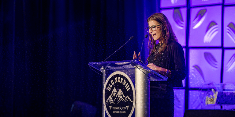 Young female Vector representative speaking at podium during Vector Marketing's annual conference