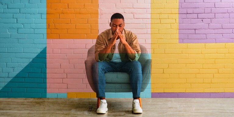 young man sitting in a chair, pensive and thinking, against brightly colored wall