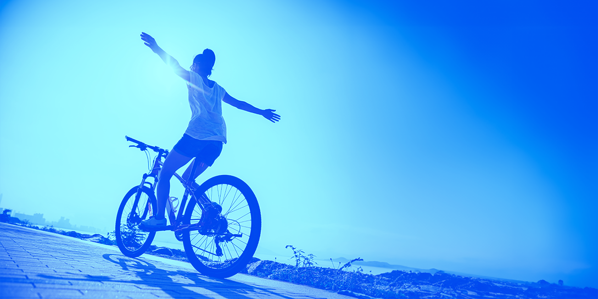 back of young woman riding a bike with her arms spread out in the air, going up a hill