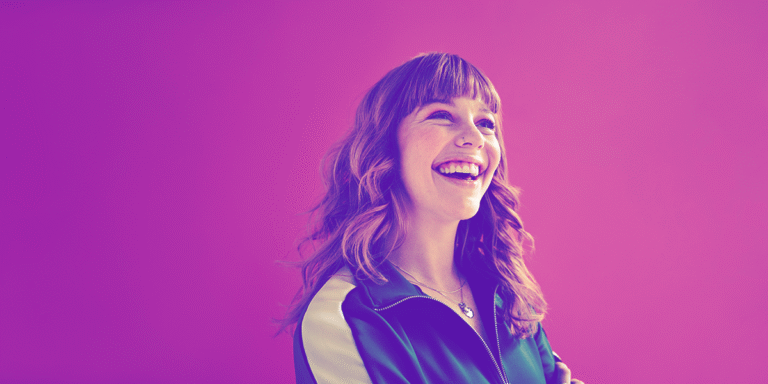 Young woman looking up and smiling with a bright pinkish purple background