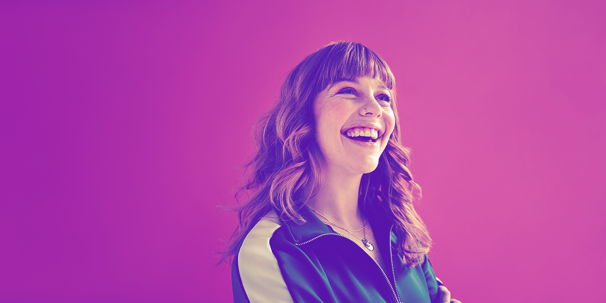 Young woman looking up and smiling with a bright pinkish purple background