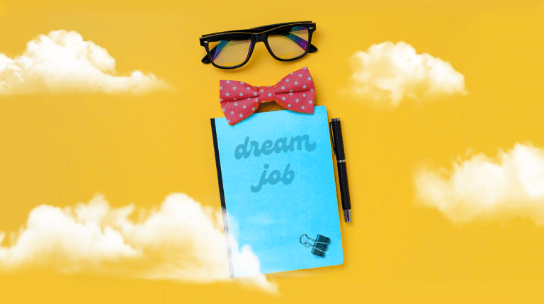 Notebook that says "dream job" with a bowtie above it and a pair of glasses on a bright yellow background with fluffy white clouds