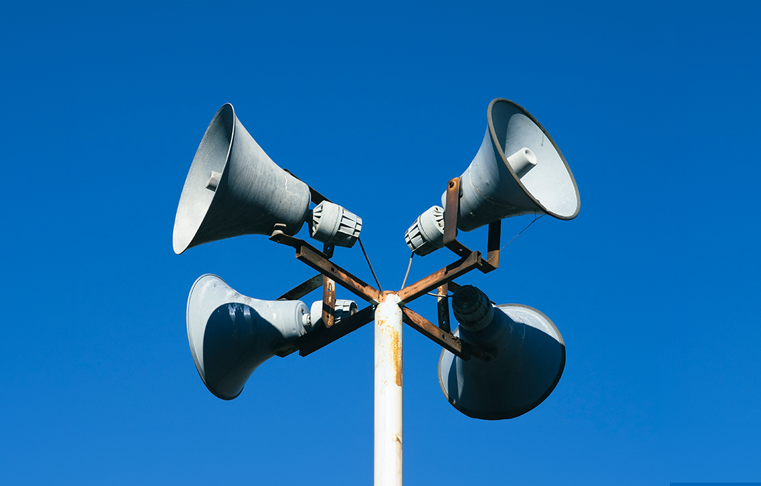 A pole with 4 megaphones against a bright blue sky