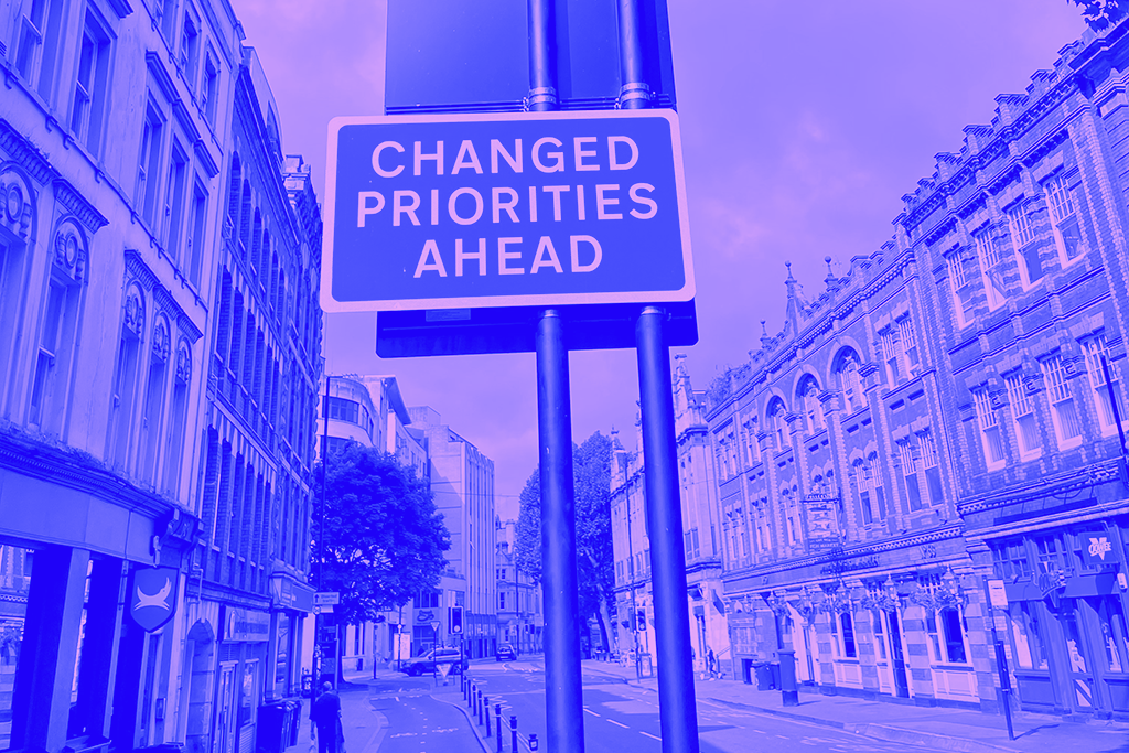 Purple duotone image of a city with a sign reading "changed priorities ahead"