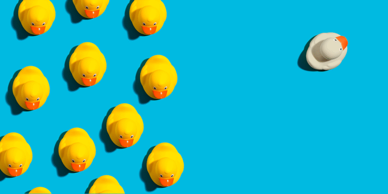 Group of rubber ducks on the left. One lone duck on the right. Set against a bright blue background.