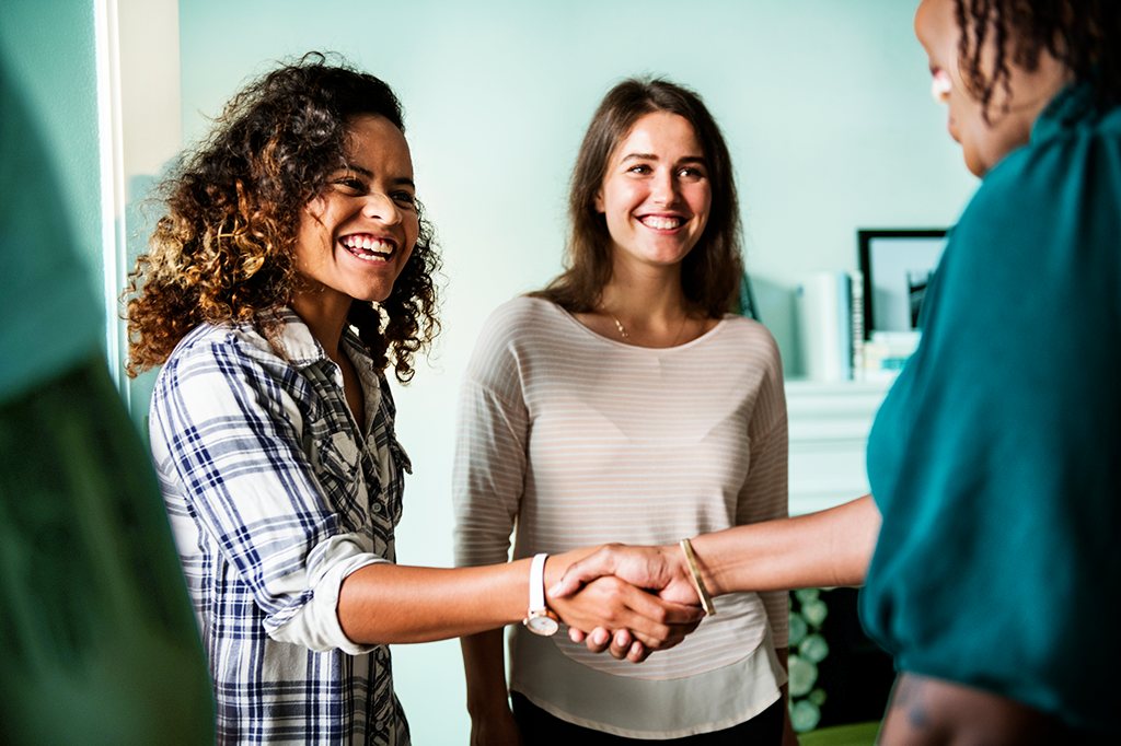 A young. woman shakes another woman's hand